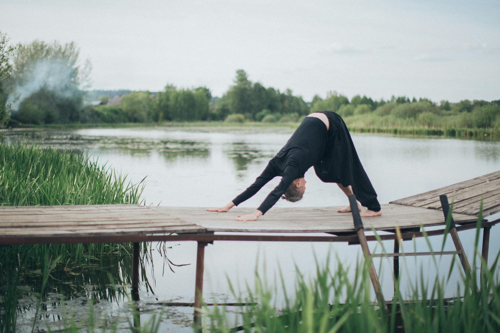 A man performs yoga by a peaceful lakeside on a wooden pier during daytime.